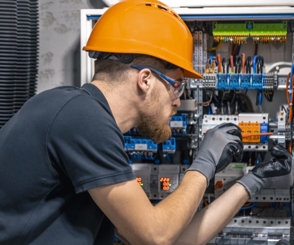 Male electrician working in a switchboard with fuses. Installation and connection of electrical equipment. Professional with tools in hand.